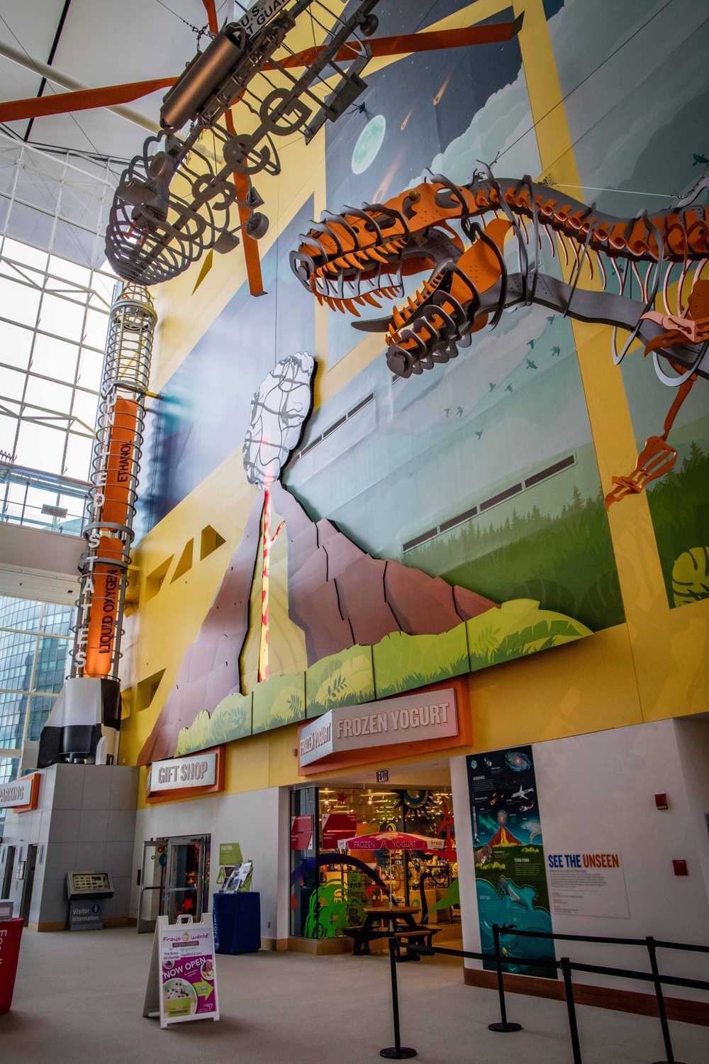 A tall atrium space with sculptures of a tornado, a rainstorm, a helicopter and a t-rex.