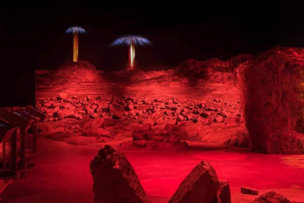 Scenic rock work in the foreground and a cgi landscape of Io in the background featuring animated volcanic eruptions.